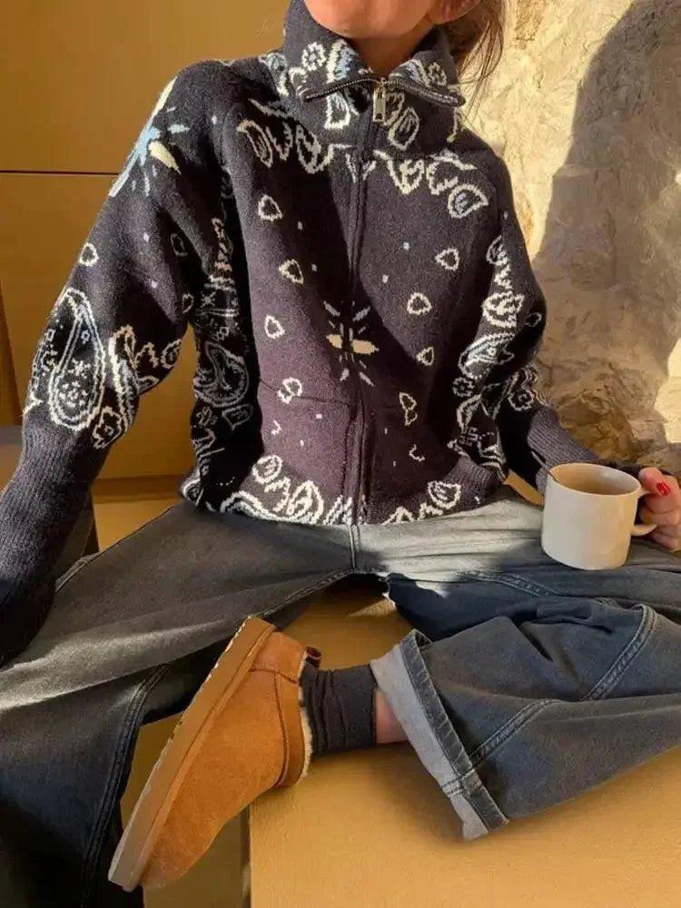 Woman wearing cozy bandana print zip-up sweater with jeans and tan boots, holding coffee mug