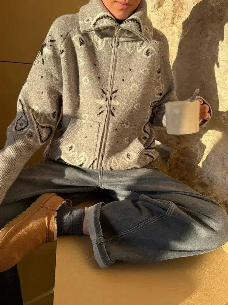 Woman in cozy patterned zip-up sweater, wide-leg jeans, and brown boots holding coffee mug