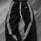 Black women's track pants with white side stripes and drawstring waist, laid on wood floor
