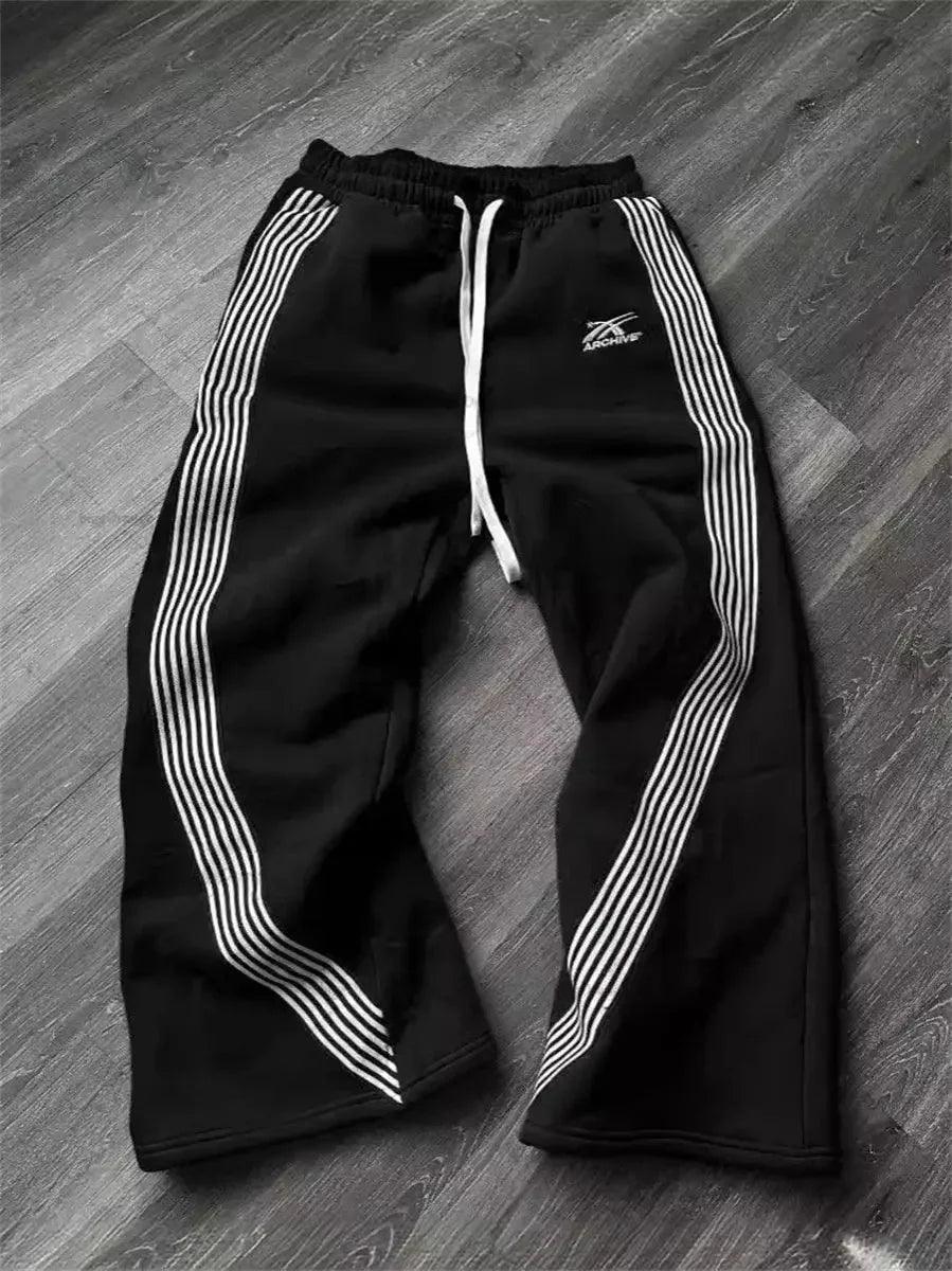 Black women's track pants with white side stripes and drawstring waist, laid on wood floor