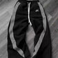 Black women's track pants with white side stripes and drawstring waist, laid on wood floor
