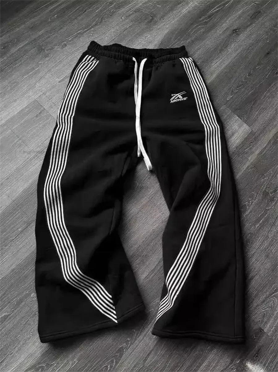 Black women's track pants with white side stripes and drawstring waist, laid on wood floor
