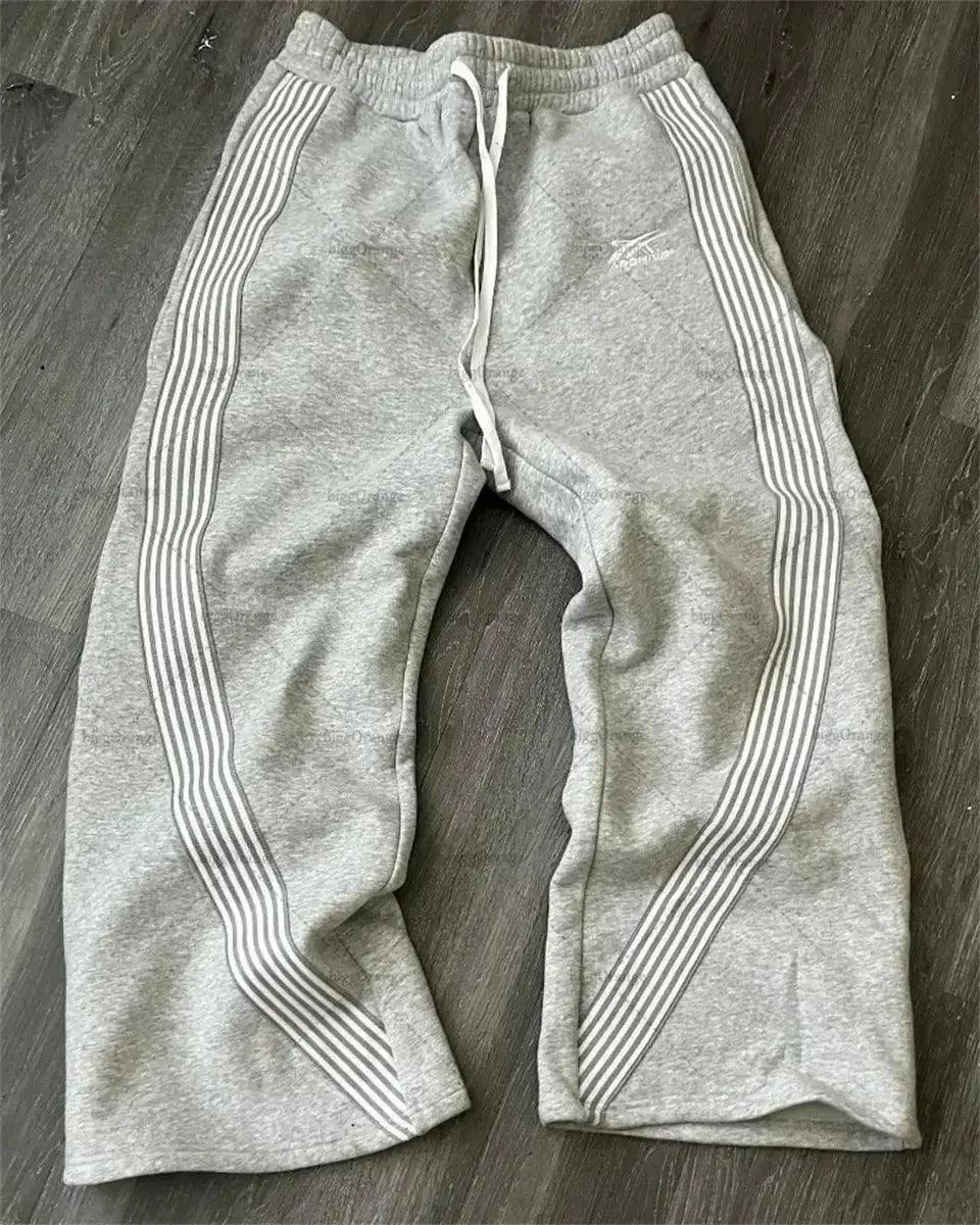 Gray women's sweatpants with white side stripes, drawstring waist, laid on wood floor