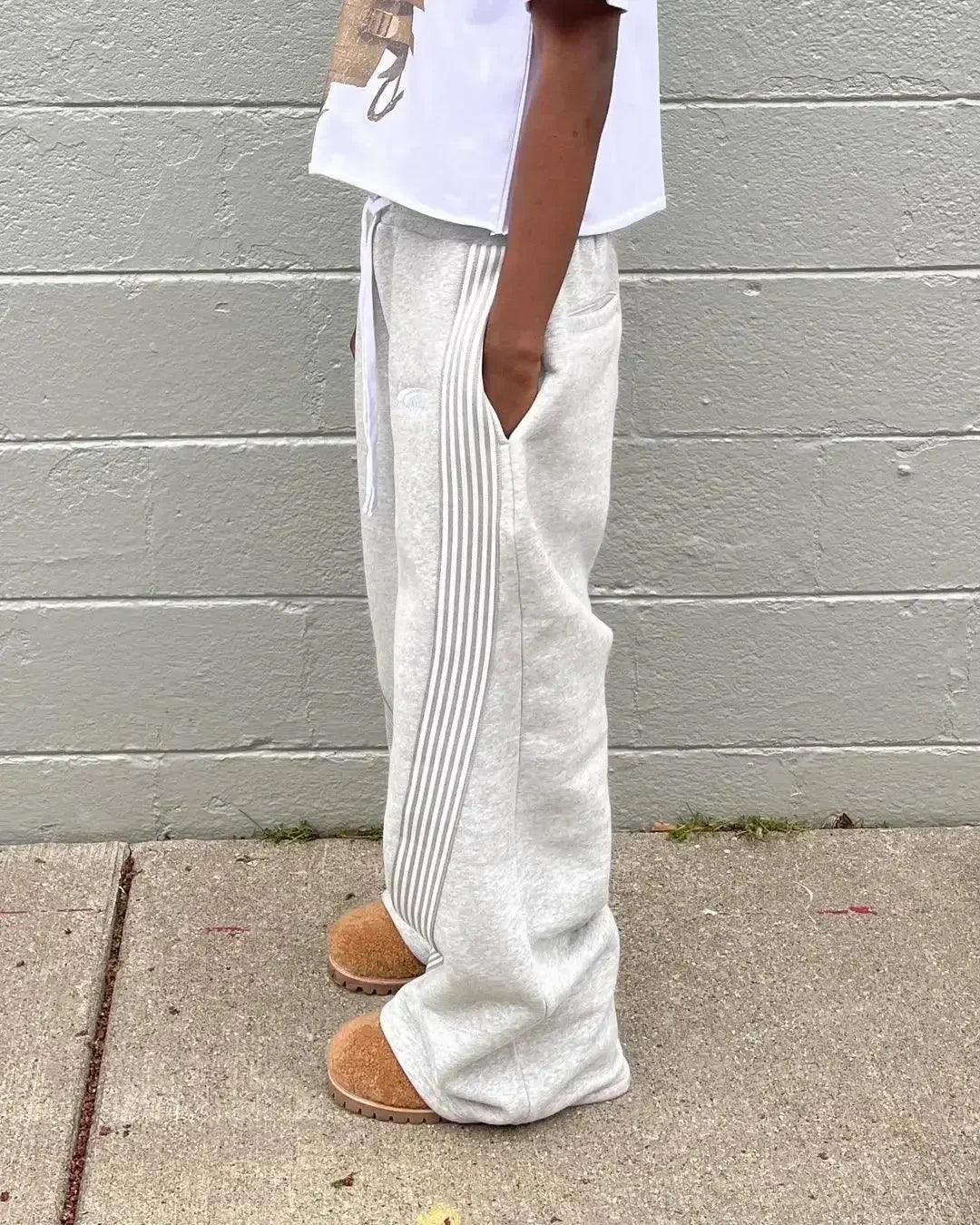 Gray striped sweatpants with side stripes, paired with cozy slippers, ideal for casual fashion.