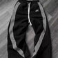 Black women's track pants with white side stripes and drawstring waist, laid on wood floor