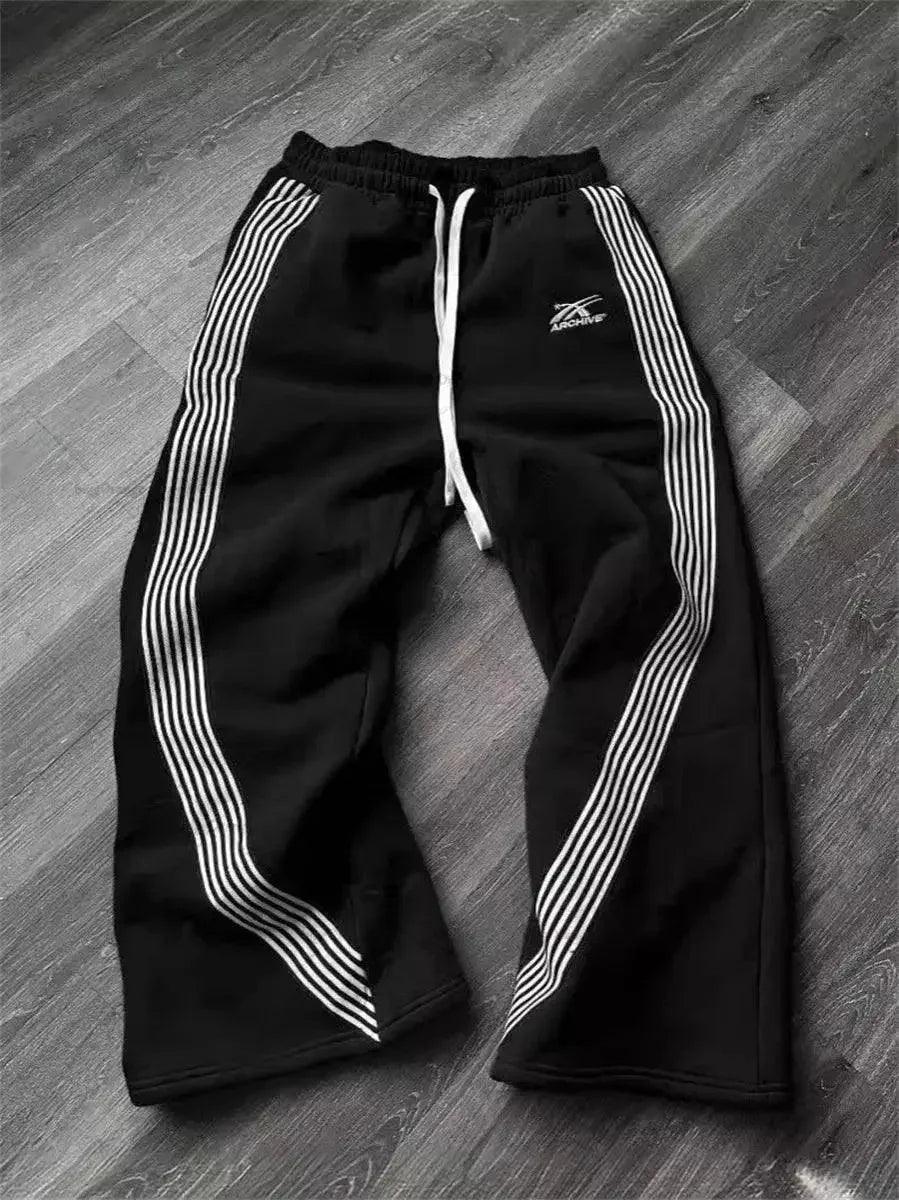 Black women's track pants with white side stripes and drawstring waist, laid on wood floor
