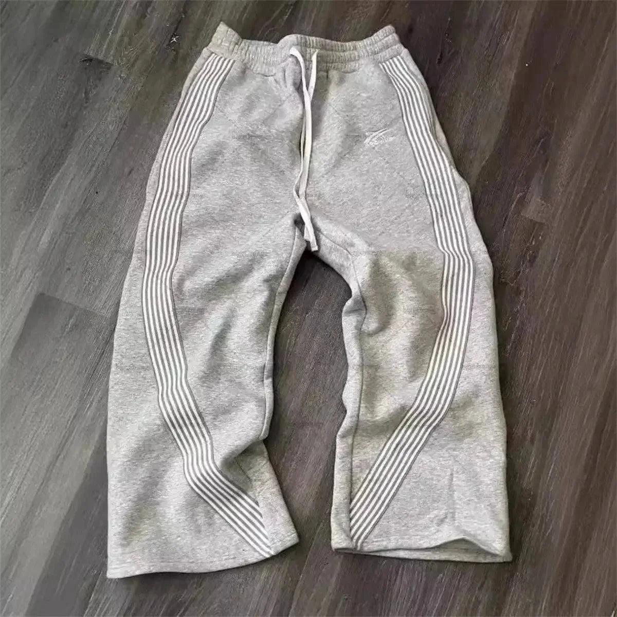 Gray women's sweatpants with side stripes, drawstring waist, laid on wood floor