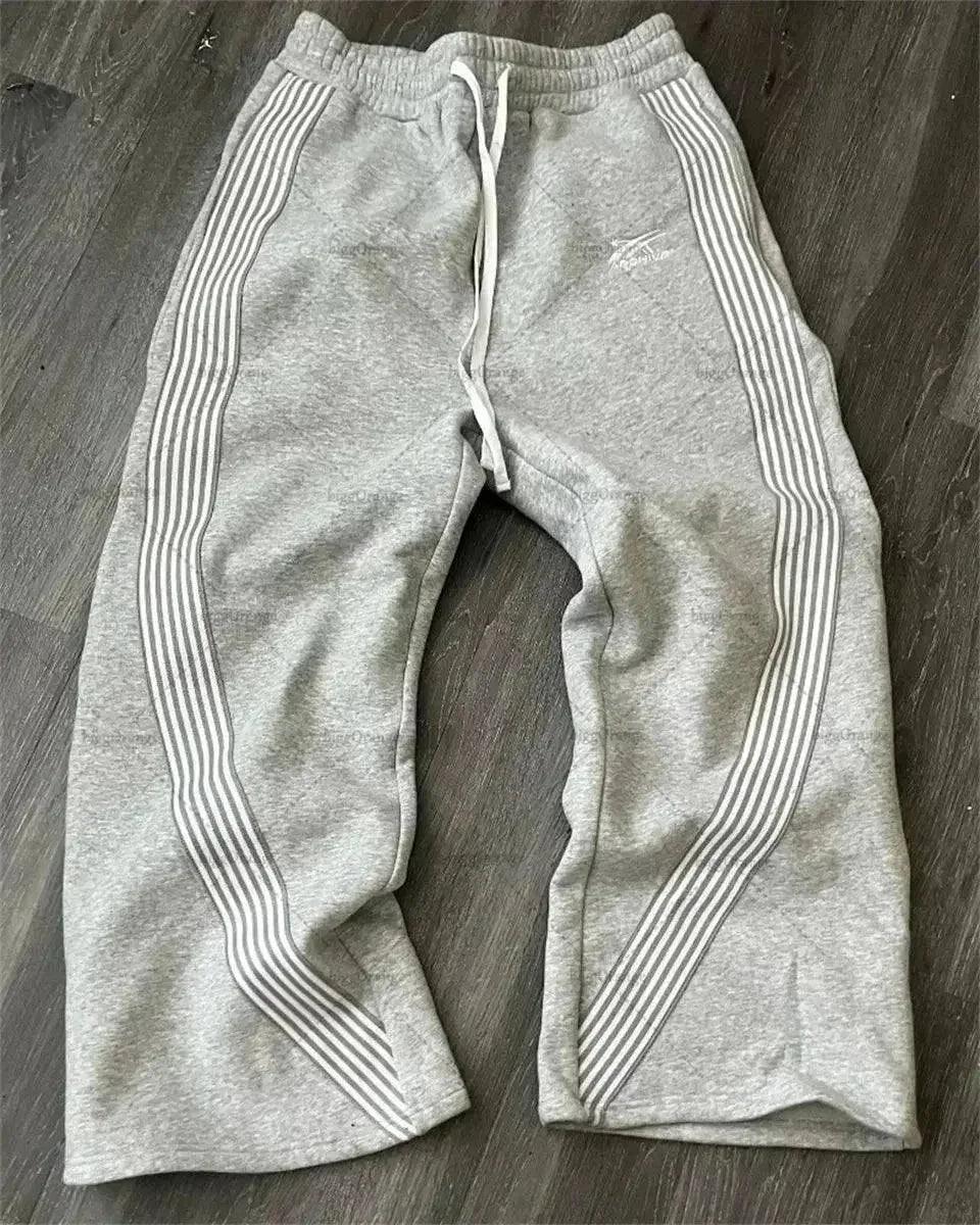 Gray women's sweatpants with white side stripes, drawstring waist, laid on wood floor