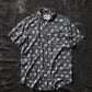 Dark gray short sleeve button-up shirt with skull and bowl print, laid flat on textured black background