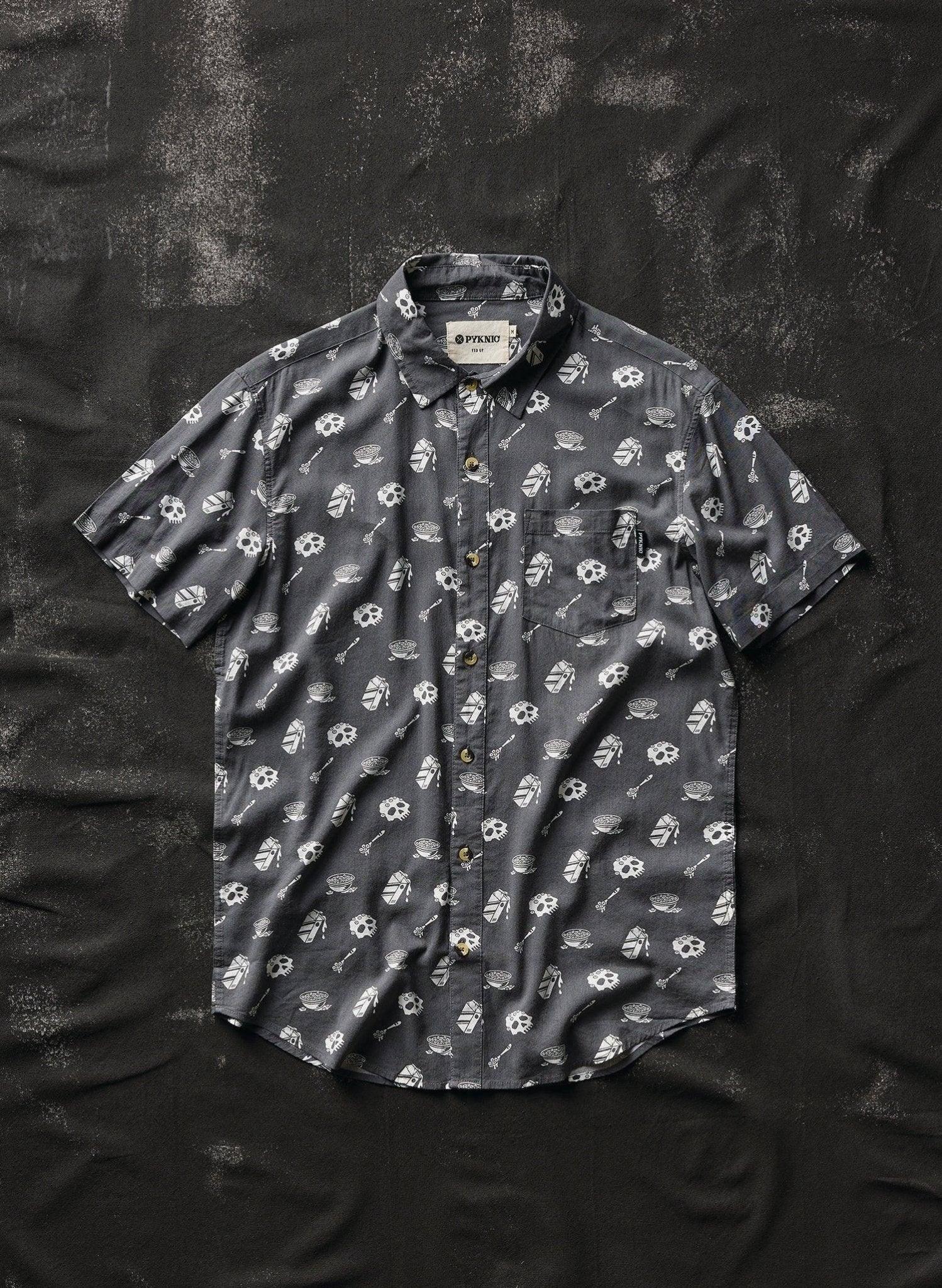 Dark gray short sleeve button-up shirt with skull and bowl print, laid flat on textured black background
