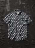 Dark gray short sleeve button-up shirt with skull and bowl print, laid flat on textured black background