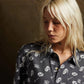 Blonde woman wearing edgy black button-up shirt with skull and bowl print, fashion style