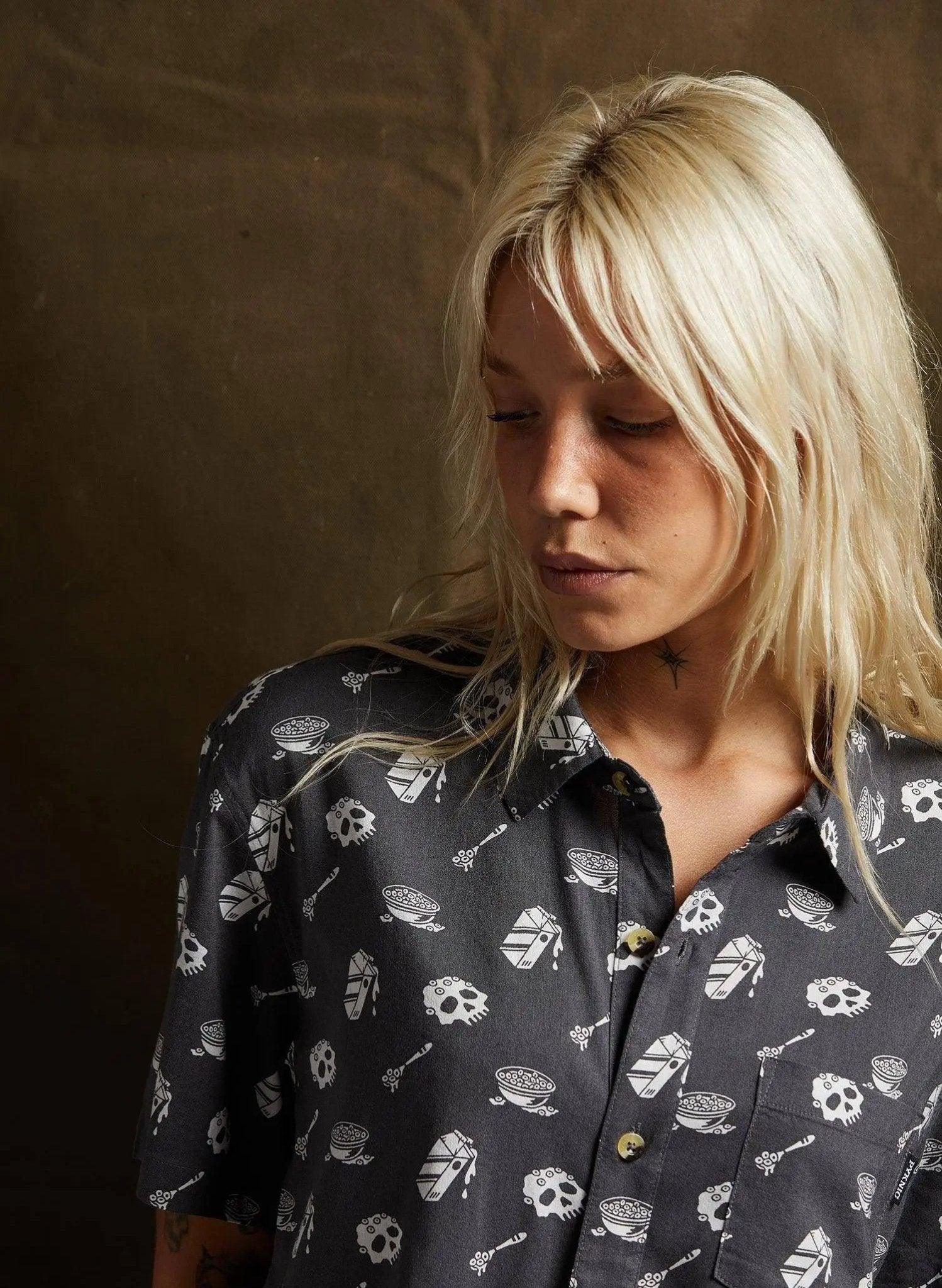 Blonde woman wearing edgy black button-up shirt with skull and bowl print, fashion style