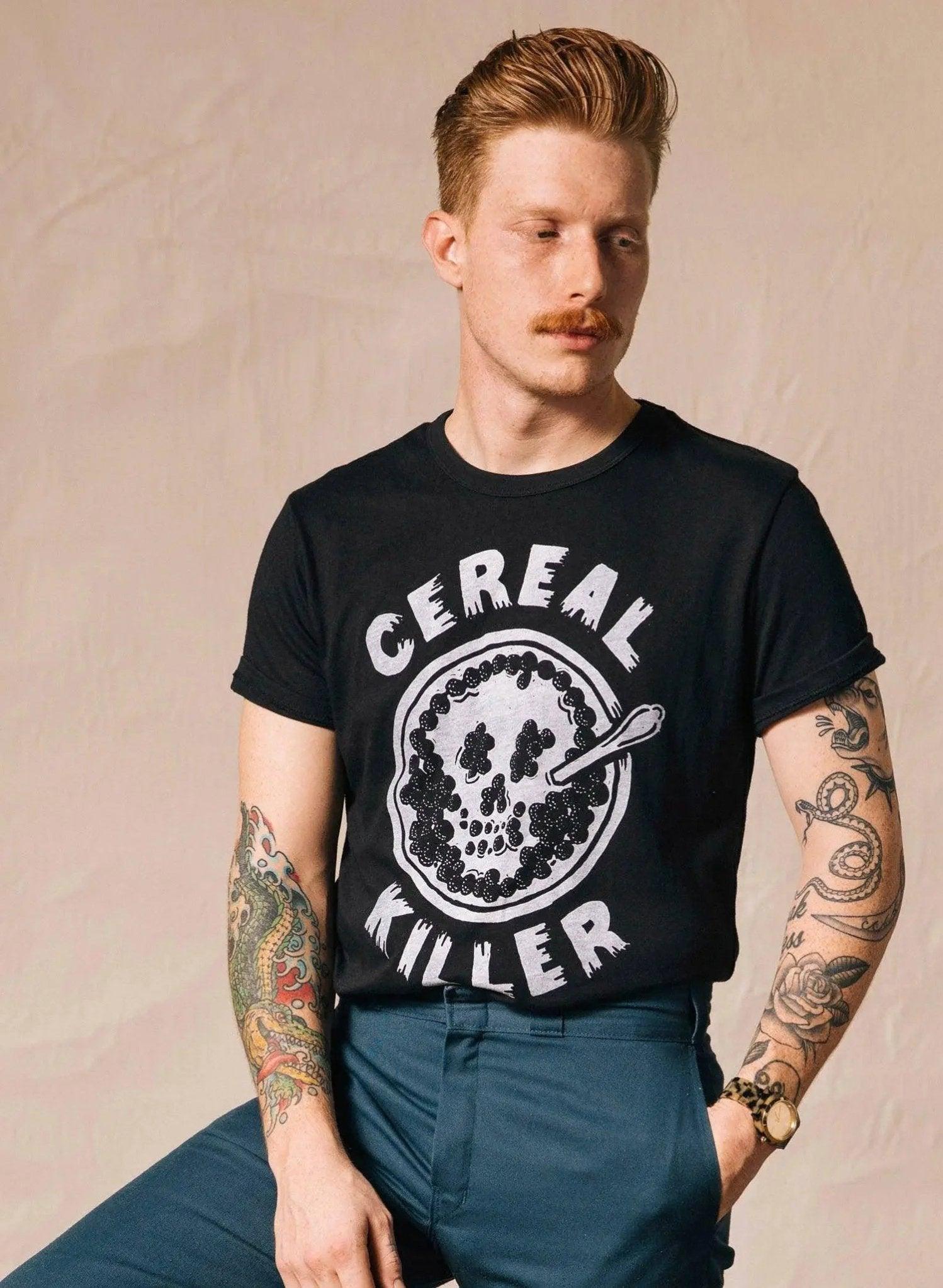 Man wearing black 'Cereal Killer' graphic tee with tattoos, styled for men's fashion