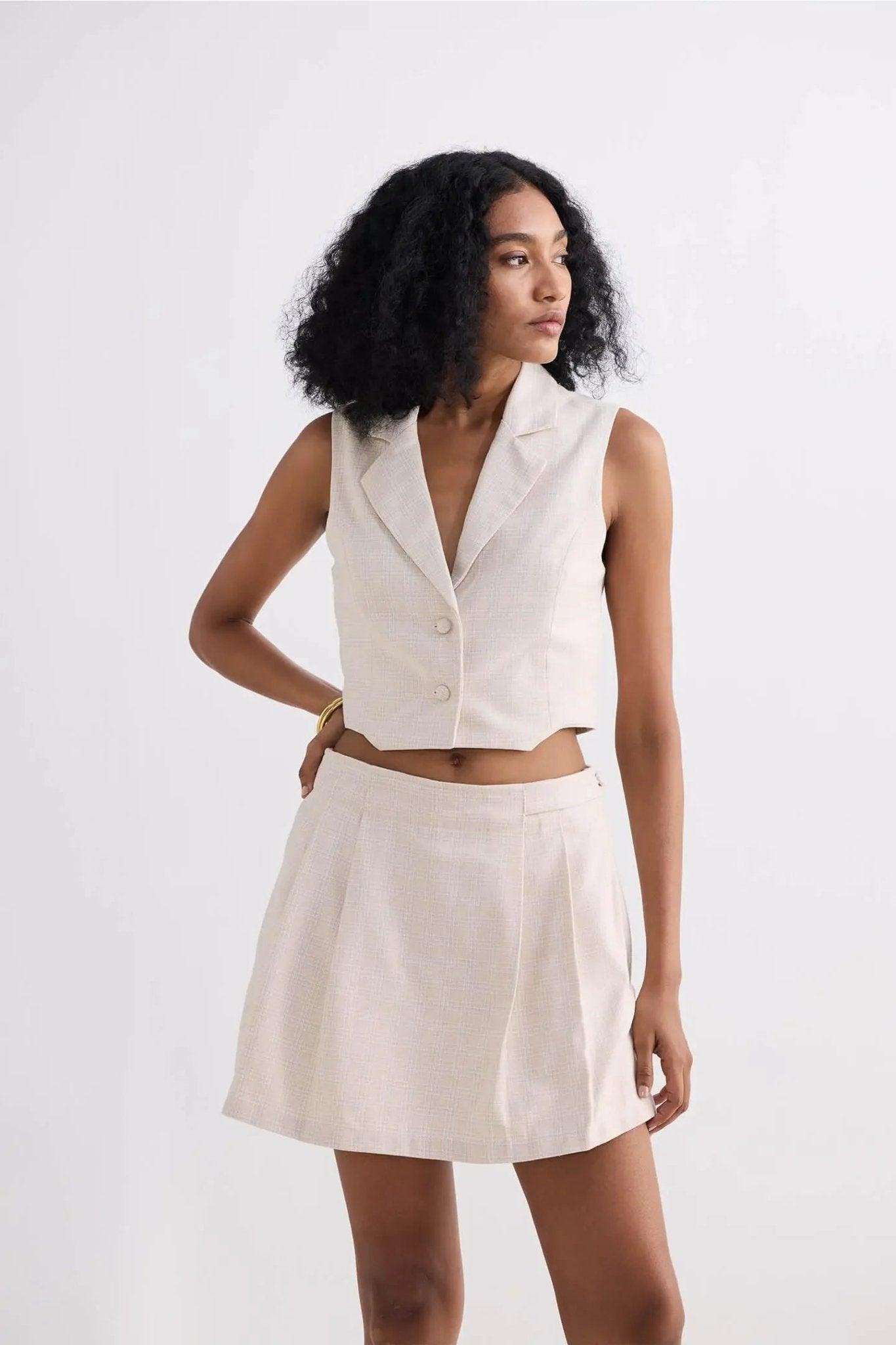 Woman in cream sleeveless blazer vest and pleated mini skirt, stylish summer fashion set