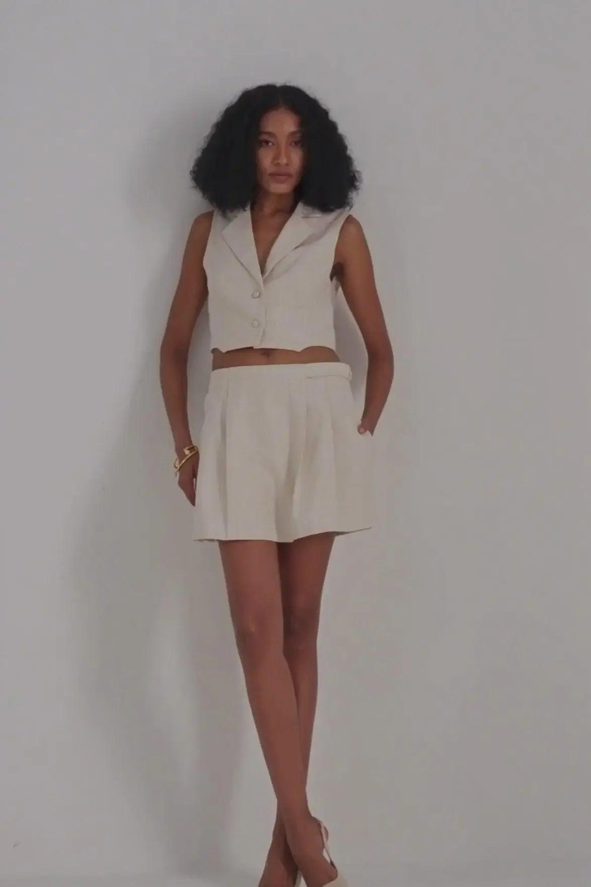 Woman in cream sleeveless cropped blazer and matching pleated shorts, modern fashion set