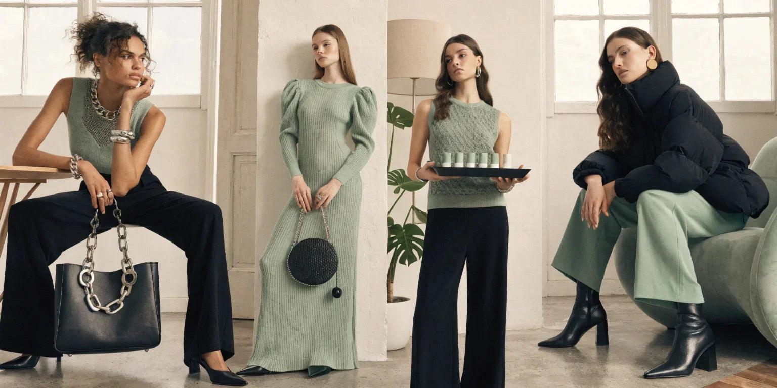 Women's fashion collection featuring green knitwear, black pants, puffer coat, and stylish handbags in modern setting