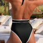 Black high-cut one-piece swimsuit with white trim, back view, beach lounge setting