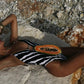 Woman in zebra print swimsuit lounging on rocks with papaya, beach fashion style