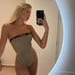 Blonde woman in houndstooth strapless bodysuit with belt, taking mirror selfie in modern bathroom