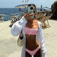 Woman in pink studded bikini with white cover-up at seaside resort, taking mirror selfie