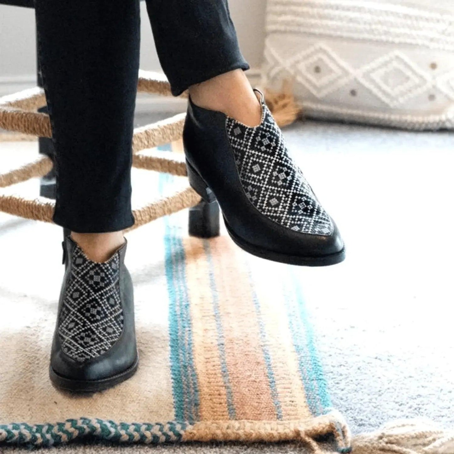 Black ankle boots with geometric pattern, worn with black pants, stylish women's fashion footwear