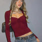 Woman in burgundy long sleeve crop top with lace trim and drawstring, paired with denim jeans and studded belt