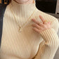 Woman in beige ribbed turtleneck sweater with gold letter L necklace and rings, red lipstick