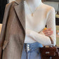 Woman in white ribbed turtleneck, herringbone blazer, and denim jeans with brown handbag