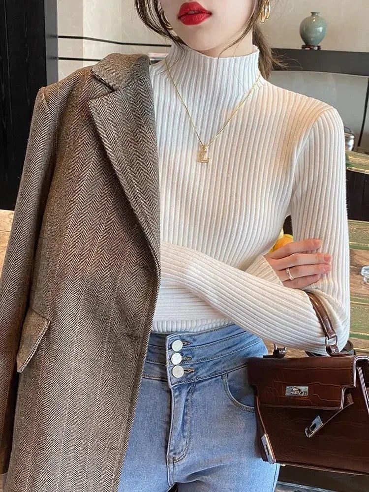 Woman in white ribbed turtleneck, herringbone blazer, and denim jeans with brown handbag