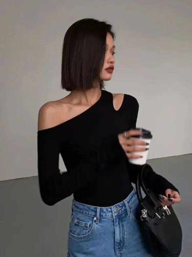 Woman in black one-shoulder top and blue jeans holding coffee, stylish fashion outfit
