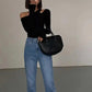 Woman in black off-shoulder top, blue jeans, and black handbag — stylish fashion outfit