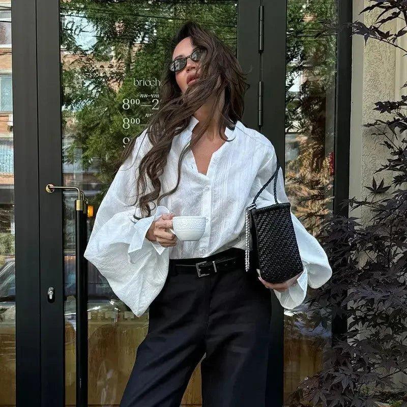 Woman in white blouse and black pants holding coffee cup, stylish streetwear fashion outfit