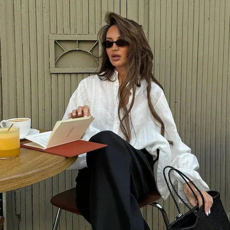 Woman in white blouse and black pants reading at café, stylish sunglasses and handbag, fashion outfit