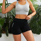 Woman in gray sports bra and black gymwear shorts, posing with tropical plants background