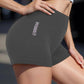 Woman modeling dark gray gymwear shorts with 'GYMWEAR' text, paired with white crop top for fitness fashion.