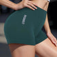 Woman modeling dark green gymwear shorts with 'GYMWEAR' text, paired with white crop top for fitness fashion.