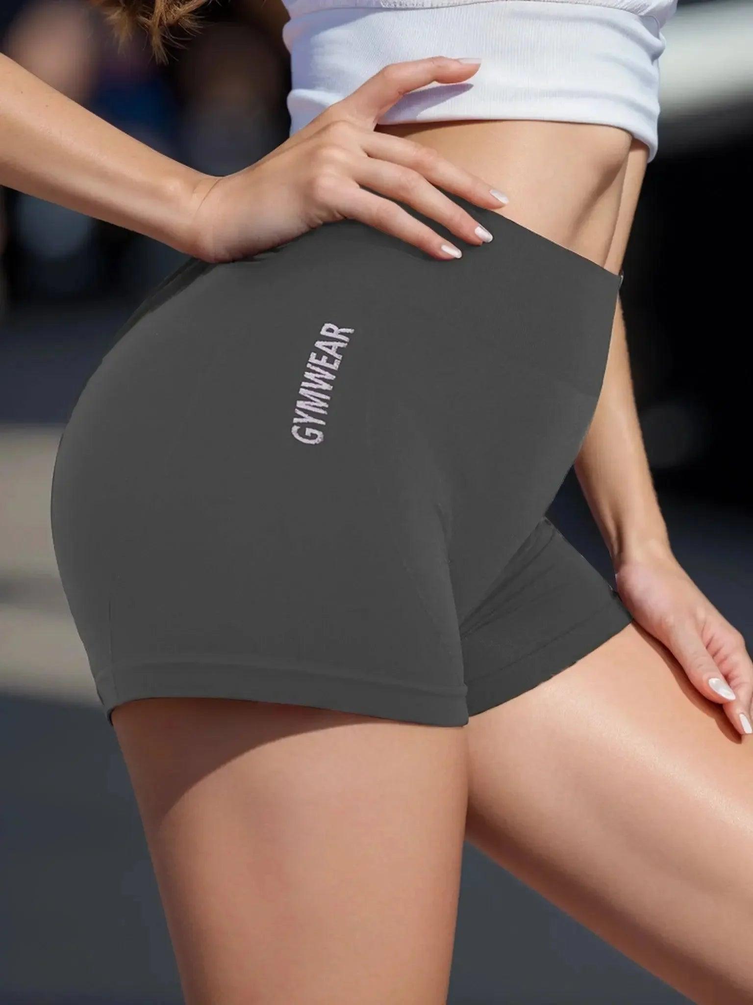 Woman wearing gray gymwear shorts with 'GYMWEAR' text, paired with white crop top for fitness fashion