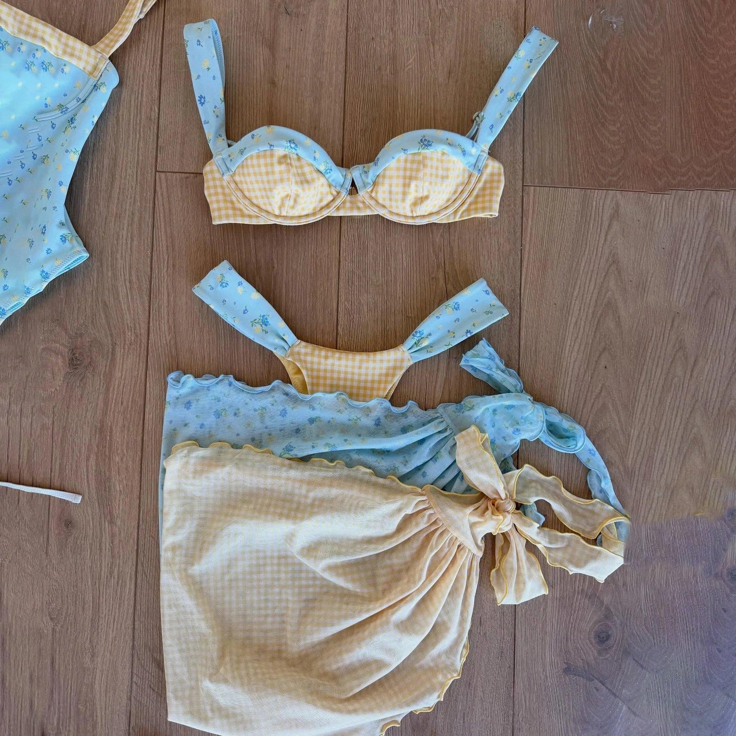 Blue and yellow floral gingham bikini set with ruffled top and tie-back, laid on wood floor