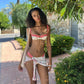 Woman in red gingham floral bikini top and matching wrap bottoms, standing outdoors under greenery