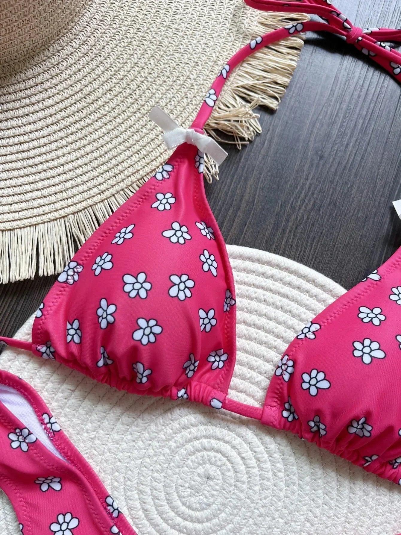 Pink floral bikini top with white daisy print, paired with straw hat on woven mat