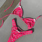 Pink floral bikini set with white daisy print, triangle top and thong bottom, laid on gray fabric