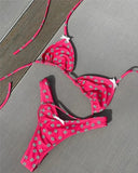 Pink floral bikini set with white daisy print, triangle top and thong bottom, laid on gray fabric