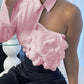Woman in pink satin one-shoulder top with floral rose detail, paired with black embellished pants