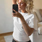 Woman taking mirror selfie in white t-shirt and black jeans, blonde wavy hair, casual fashion style