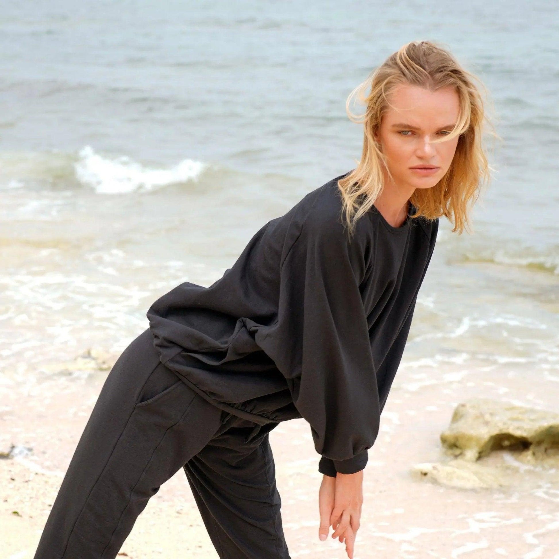 Woman in black oversized sweatshirt and joggers at beach, casual fashion