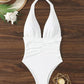 White halter neck one-piece swimsuit with ruched waist, beach hat and seashell on wood
