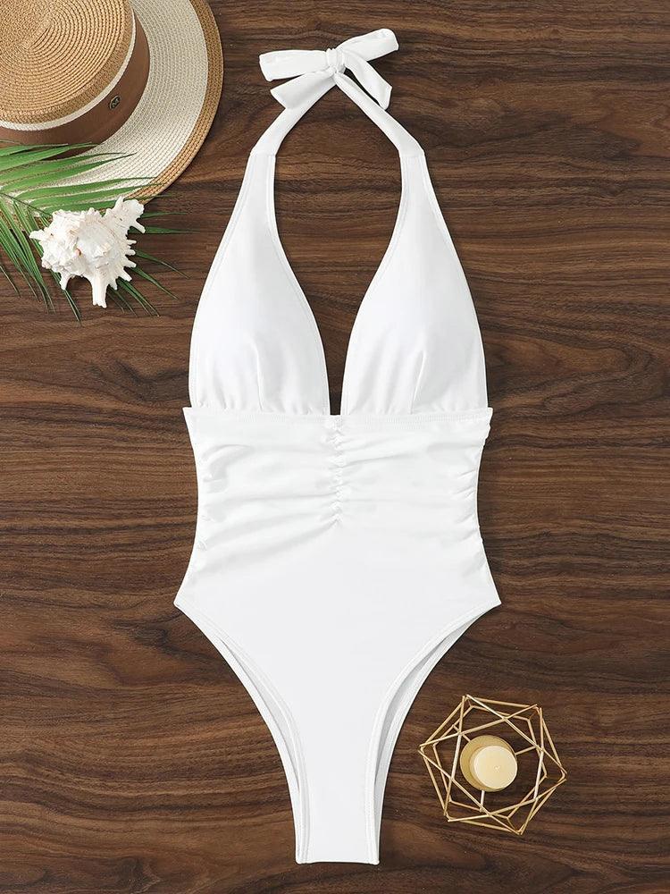 White halter neck one-piece swimsuit with ruched waist, beach hat and seashell on wood