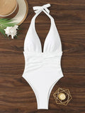 White halter neck one-piece swimsuit with ruched waist, beach hat and seashell on wood