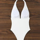 White halter neck one-piece swimsuit with tie back, laid flat on wood background